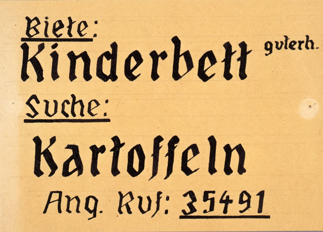 rechteckiges, gebliches Papier, mit schwarzer Tinte handbeschrieben. Biete: Kinderbett guterh. Suche: Kartoffeln. Ang. Ruf: 35491